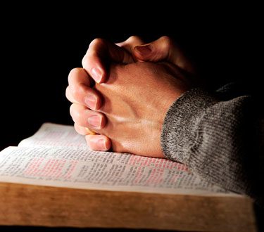 Durch Gebet helfen: Betende Hände über einer Bibel