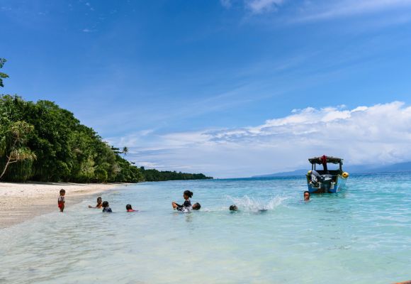 Kinder schwimmen und spielen im warmen Wasser und am Strand von Mansinam